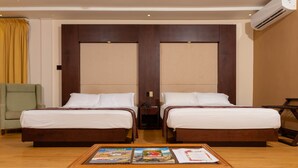 A hotel room with two beds, a wooden headboard, a wicker coffee table with magazines, and a chair. - Herdmanston Lodge (Georgetown)