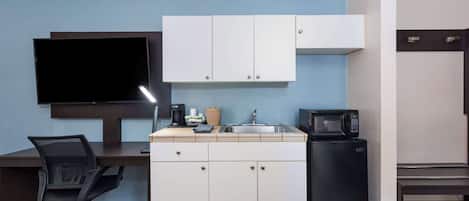 Una kitchenette compacta con televisión de pantalla plana, microondas y refrigerador pequeño.