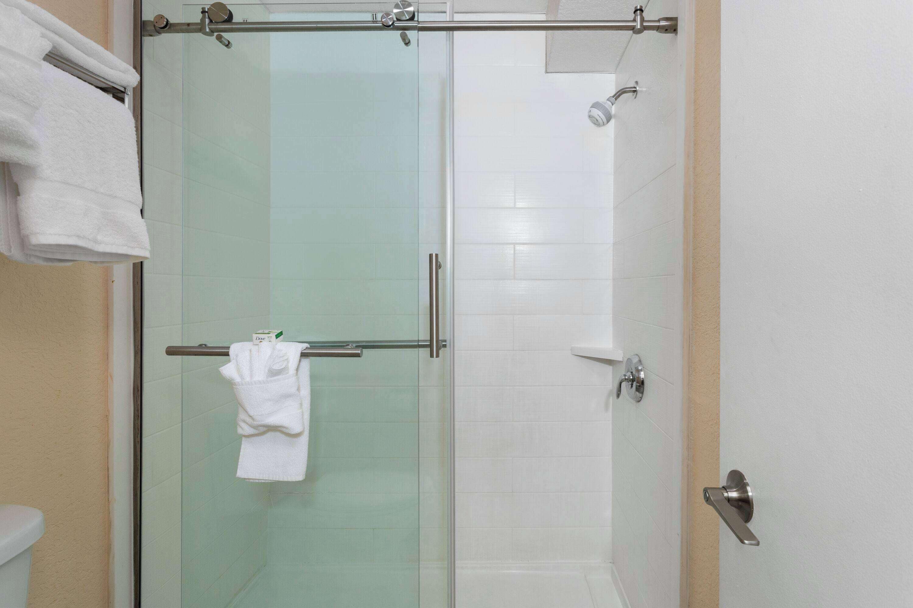 A glass-enclosed shower stall with a towel rack and a handheld showerhead.
