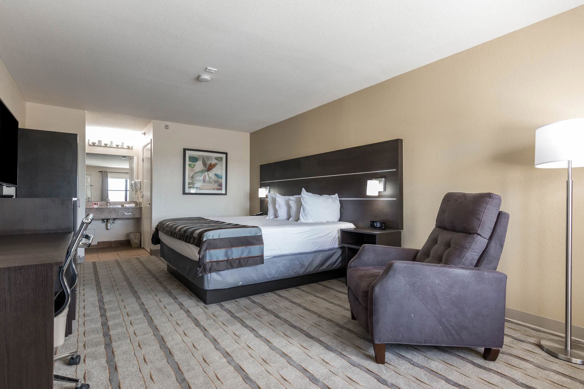 Une chambre d’hôtel avec un lit, une chaise, un bureau, une lampe et, au fond, une salle de bain.