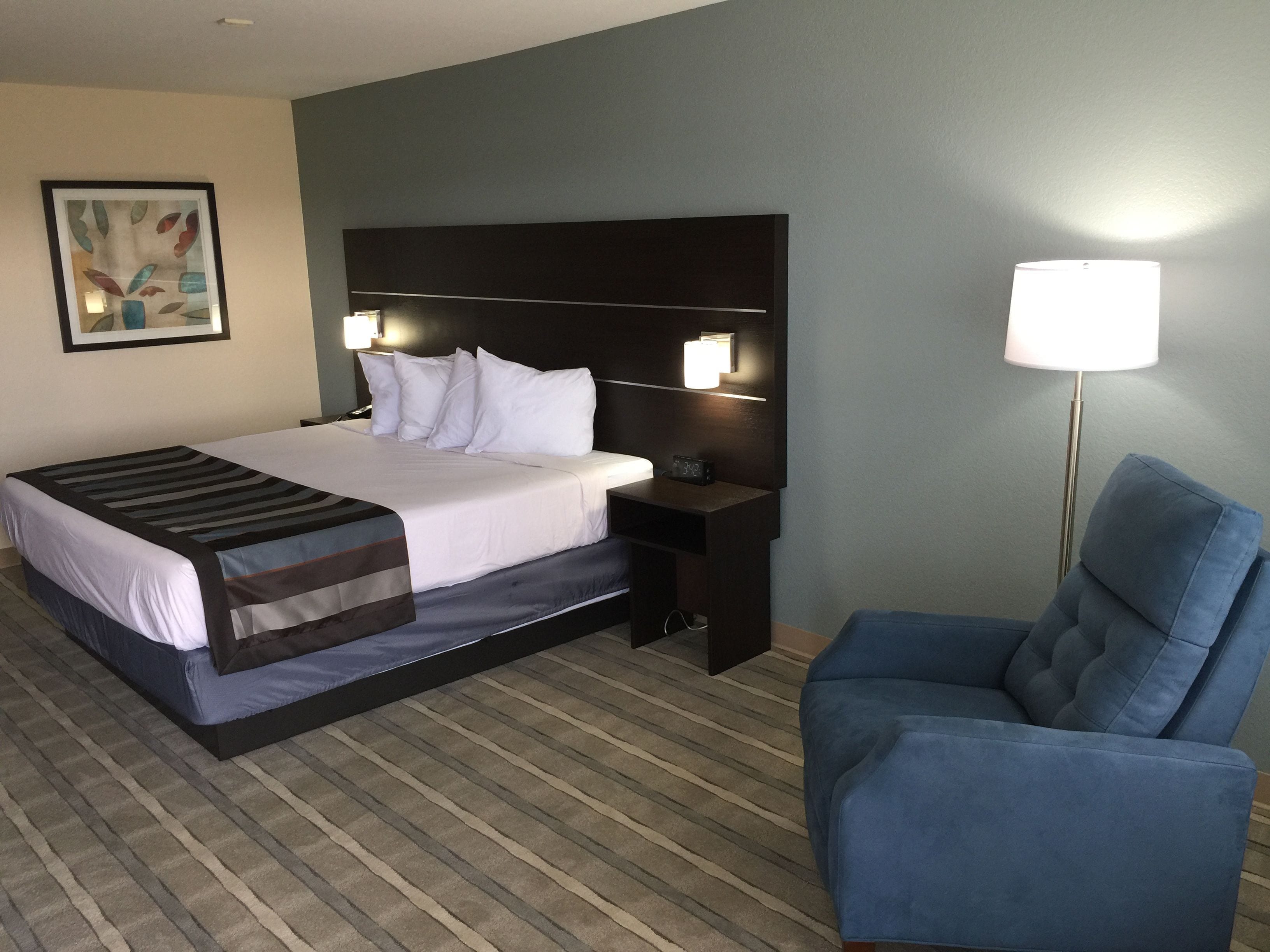 A hotel room with a bed, a nightstand, a lamp, and a chair.
