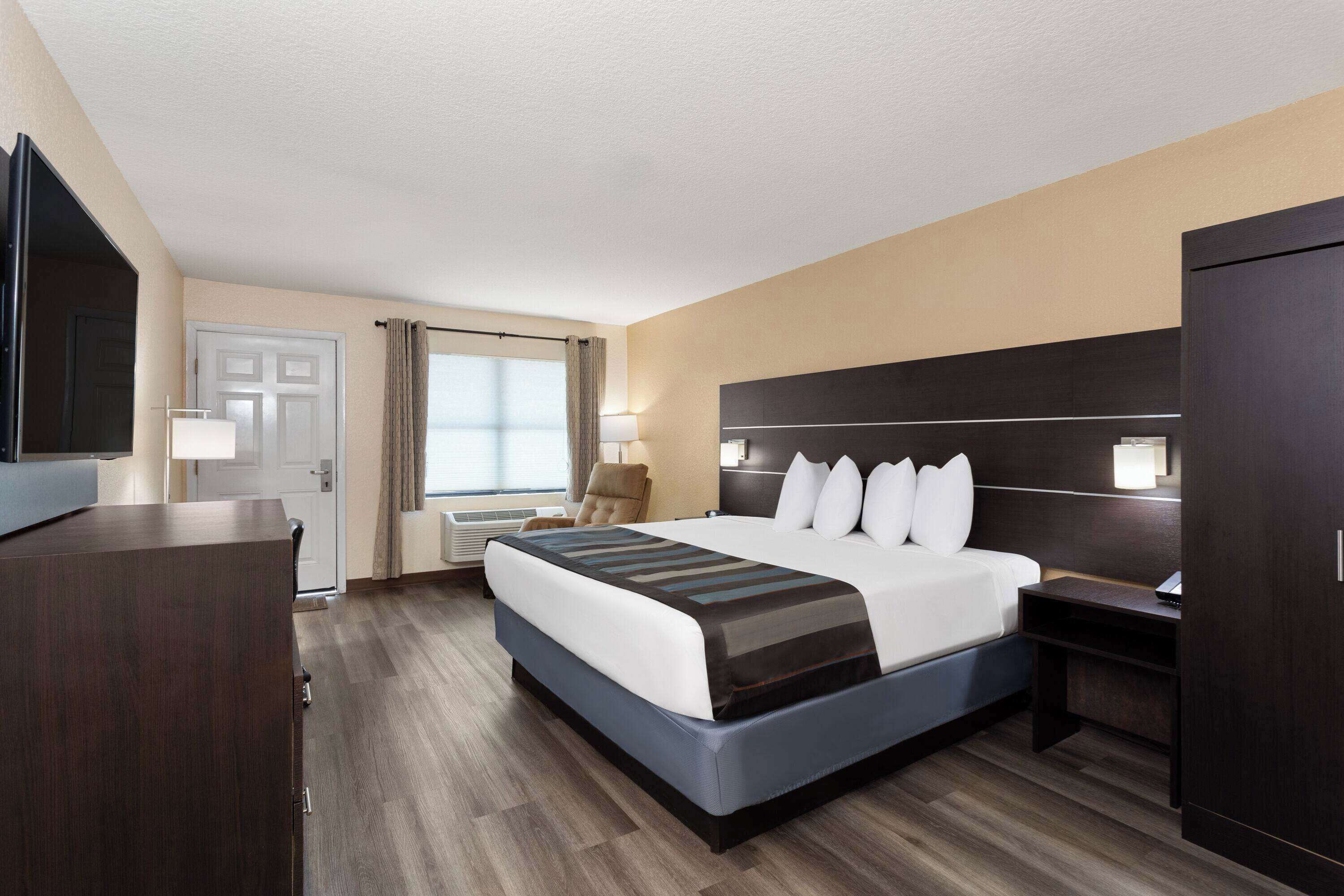 A hotel room with a large bed, a desk, a chair, a TV, and a wardrobe.