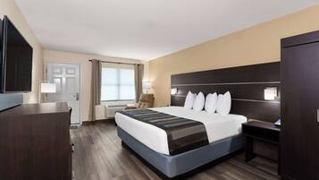 A hotel room with a large bed, a desk, a chair, a TV, and a wardrobe.
