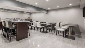 A modern dining area with multiple tables and chairs, a counter with a display, and recessed ceiling lights. - Baymont by Wyndham Punta Gorda/Port Charlotte (Punta Gorda)