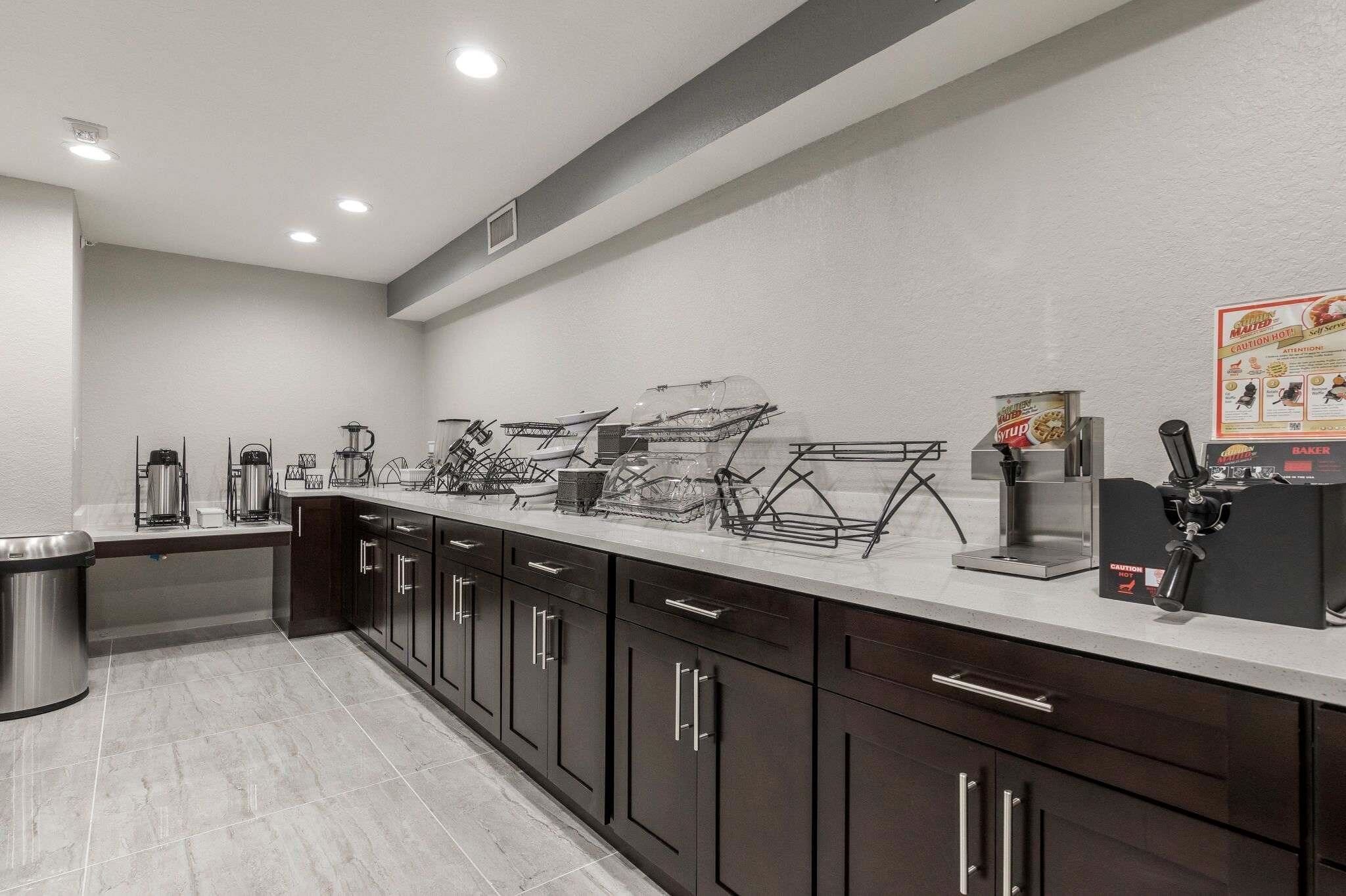 A modern kitchen with dark cabinets, a stainless steel sink, and a coffee station.