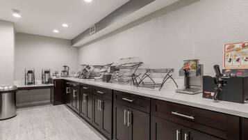 A modern kitchen with dark cabinets, a stainless steel sink, and a coffee station.