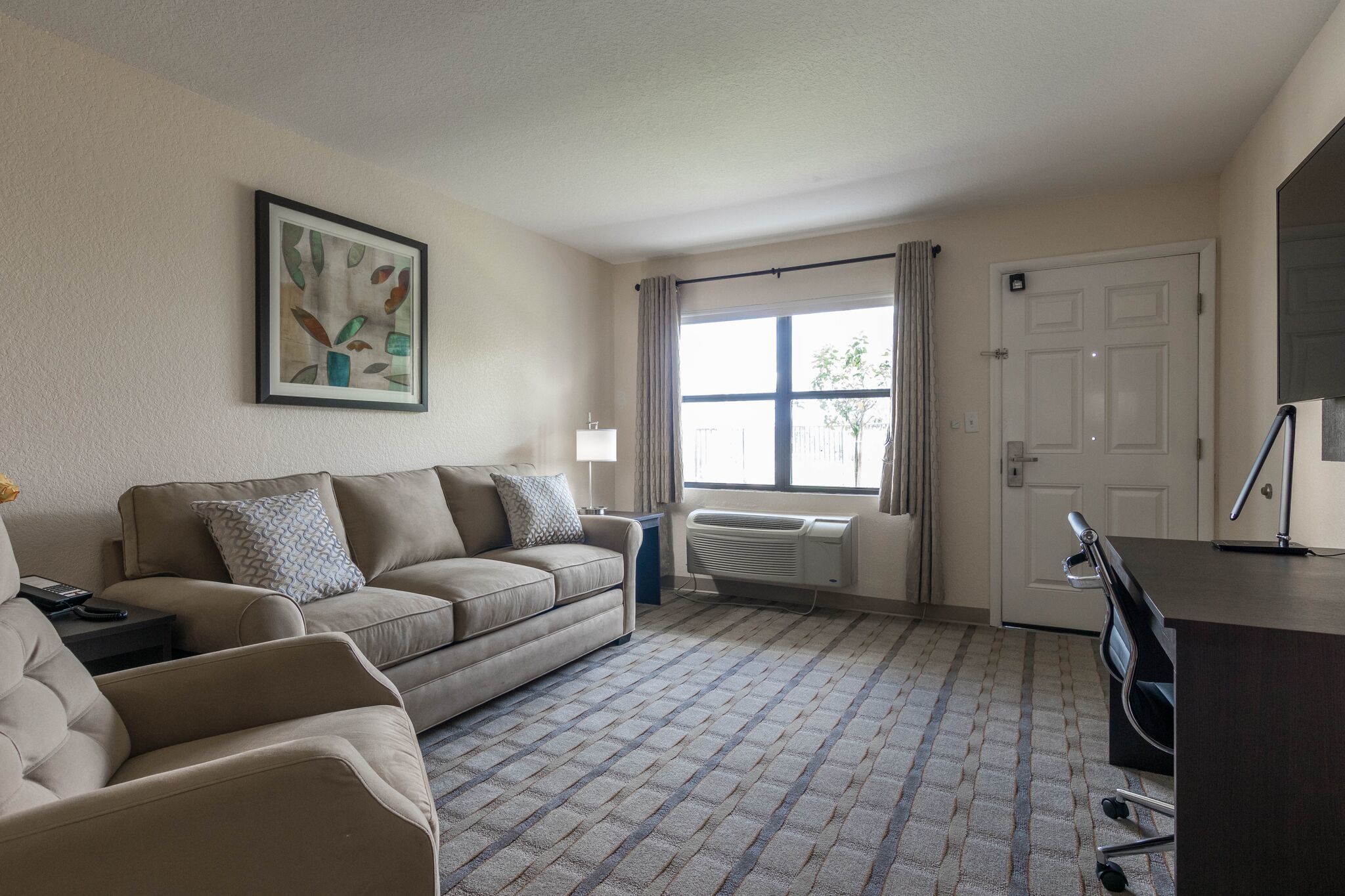 A living room with a beige sofa, a small table, a radiator, a window with curtains, and a door.