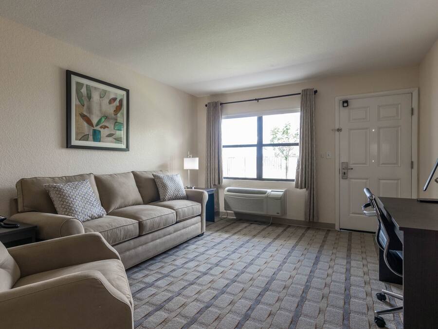 A living room with a beige sofa, a small table, a radiator, a window with curtains, and a door.