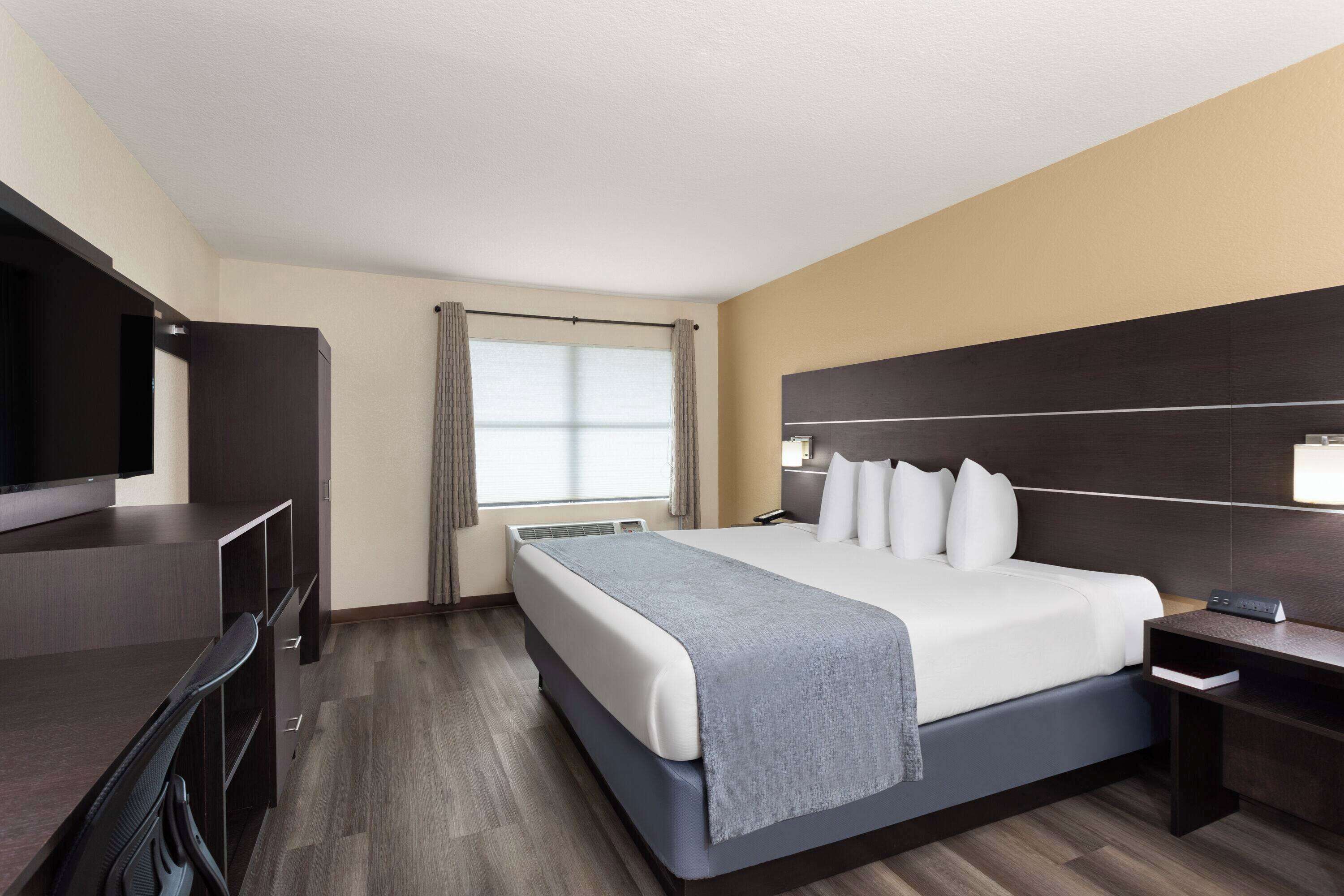 A hotel room with a large bed, a desk, a flat-screen TV, and a window with curtains.