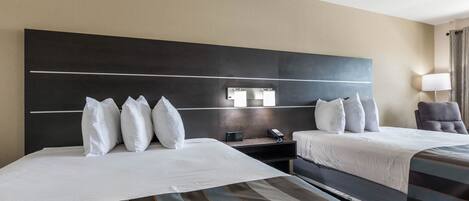 A hotel room with two beds, a large dark headboard, bedside tables, a lamp, and a view of the room.
