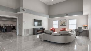 A spacious living area with a curved grey sofa, a flat-screen TV, and a dining area with chairs and a table. - Baymont by Wyndham Punta Gorda/Port Charlotte (Punta Gorda)