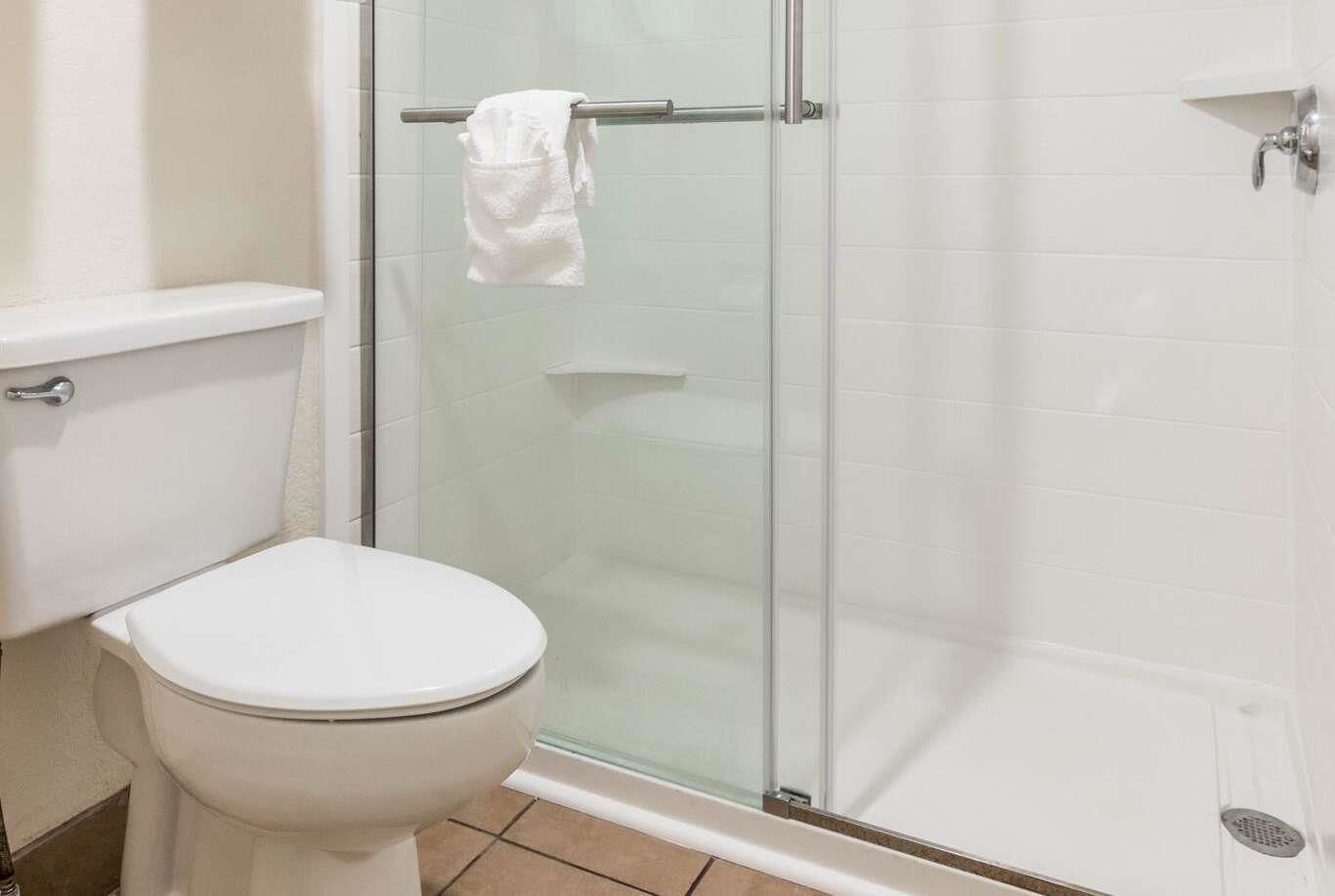 A bathroom with a toilet, a glass shower enclosure, and a white tiled wall.
