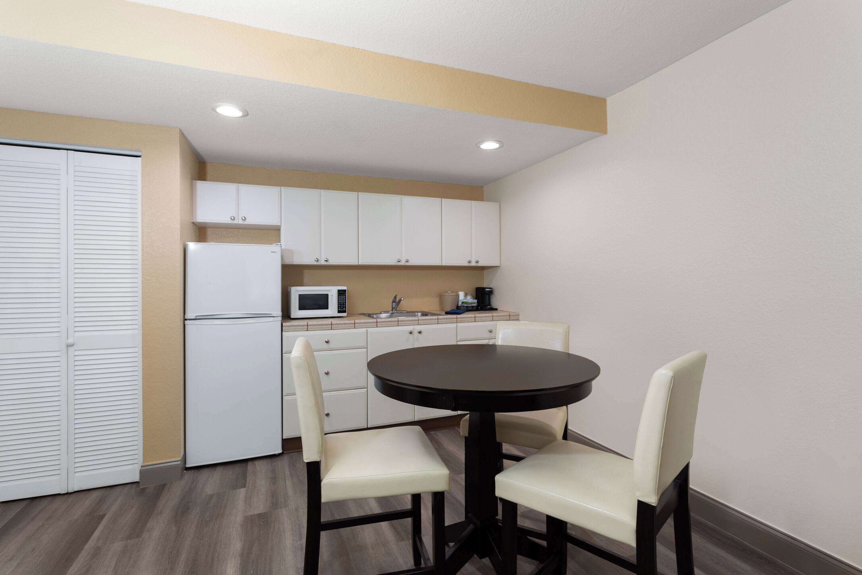 A compact kitchen with white cabinets, a microwave, and a refrigerator. There is a round table with two chairs.