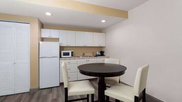 A compact kitchen with white cabinets, a microwave, and a refrigerator. There is a round table with two chairs.