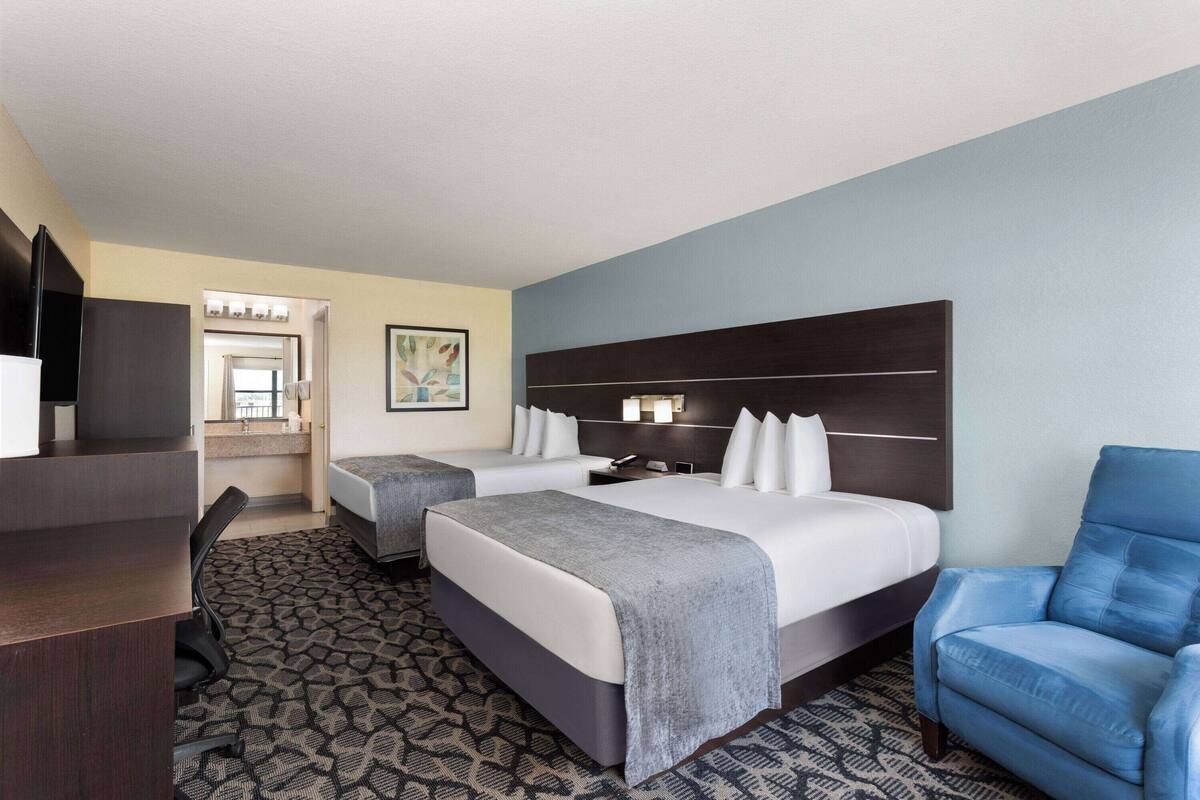 Une chambre d’hôtel avec deux lits, un bureau, une chaise et un téléviseur.