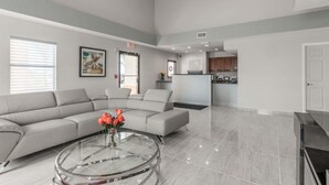 A spacious living area with a grey sectional sofa, a glass coffee table with flowers, and a kitchen in the background. - Baymont by Wyndham Punta Gorda/Port Charlotte (Punta Gorda)