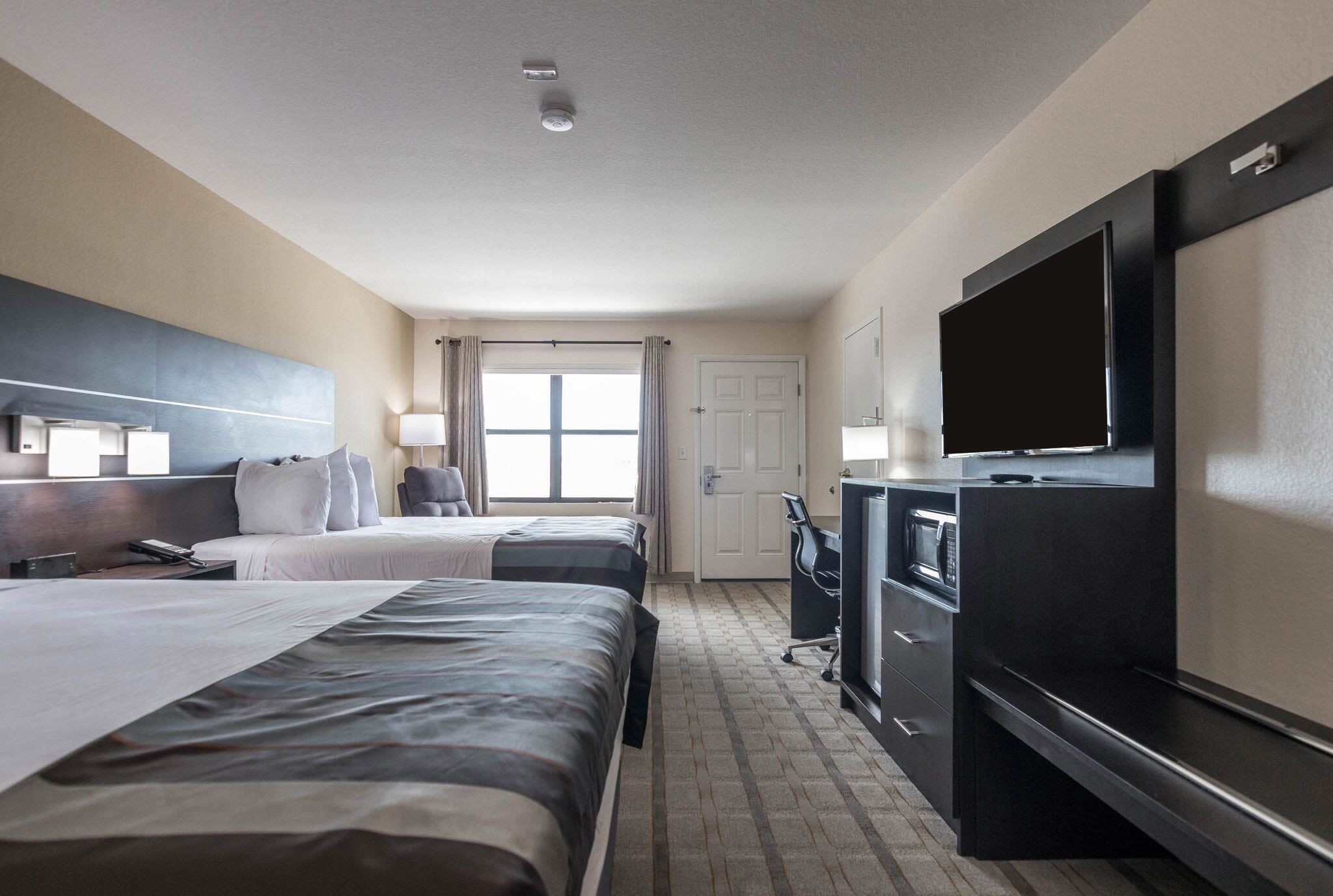A hotel room with two beds, a TV, a desk, and a window with curtains.