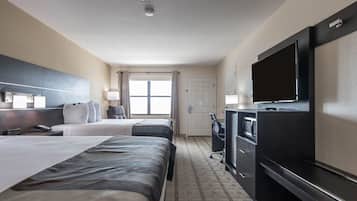 A hotel room with two beds, a TV, a desk, and a window with curtains.