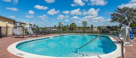 A circular pool with a metal ladder and lounge chairs around it, surrounded by a brick patio.