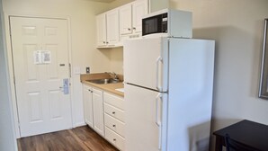 A kitchen with white cabinets, a microwave, a sink, and a refrigerator. - Stay Plus Extended Stay Suites (Auburn)