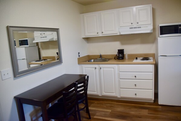 A compact kitchen with white cabinets, a microwave, a coffee maker, and a refrigerator.