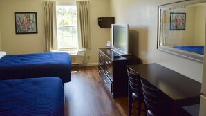 A hotel room with two beds, a desk with a television, a chair, and a window with curtains. - Stay Plus Extended Stay Suites (Auburn)