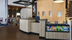 A modern reception area with a curved desk, a beverage cooler, and a seating area with a lamp and decorative items. - Hyatt Place Raleigh/Cary (Raleigh)