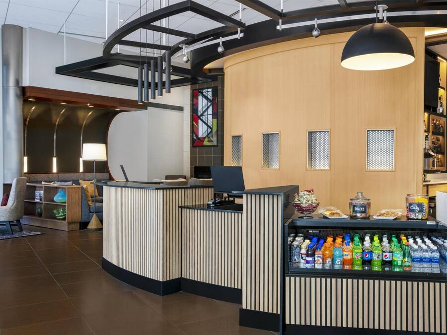 Una recepción moderna con un mostrador curvo, un refrigerador de bebidas y un área de estar con una lámpara y elementos decorativos.