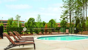 A pool area with lounge chairs, a fenced pool, and surrounding greenery.