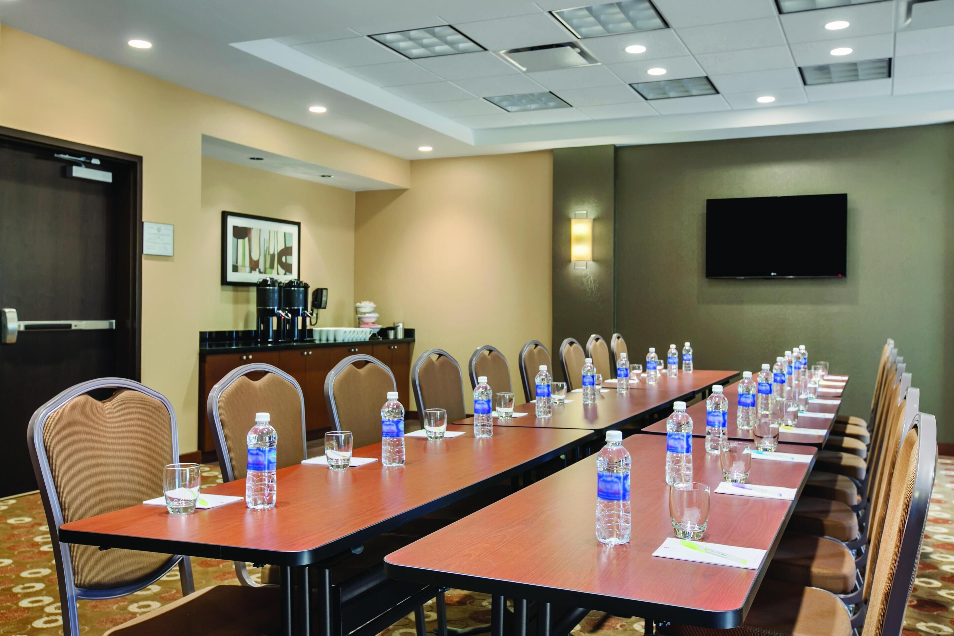 A conference room with a long table, chairs, water bottles, and a TV on the wall.