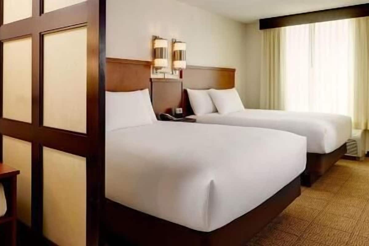 A hotel room with two beds, a wooden headboard, a nightstand, and a window with curtains.