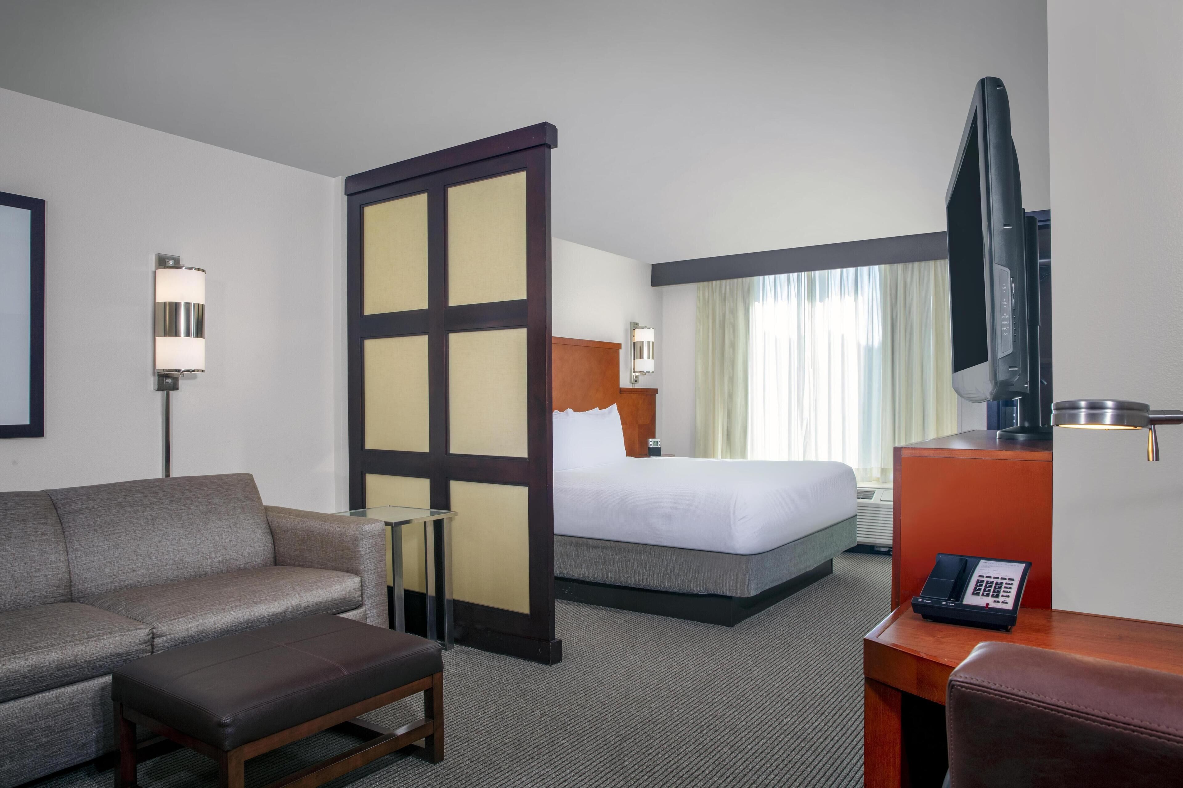 A hotel room with a bed, a sofa, a desk with a telephone, and a television.