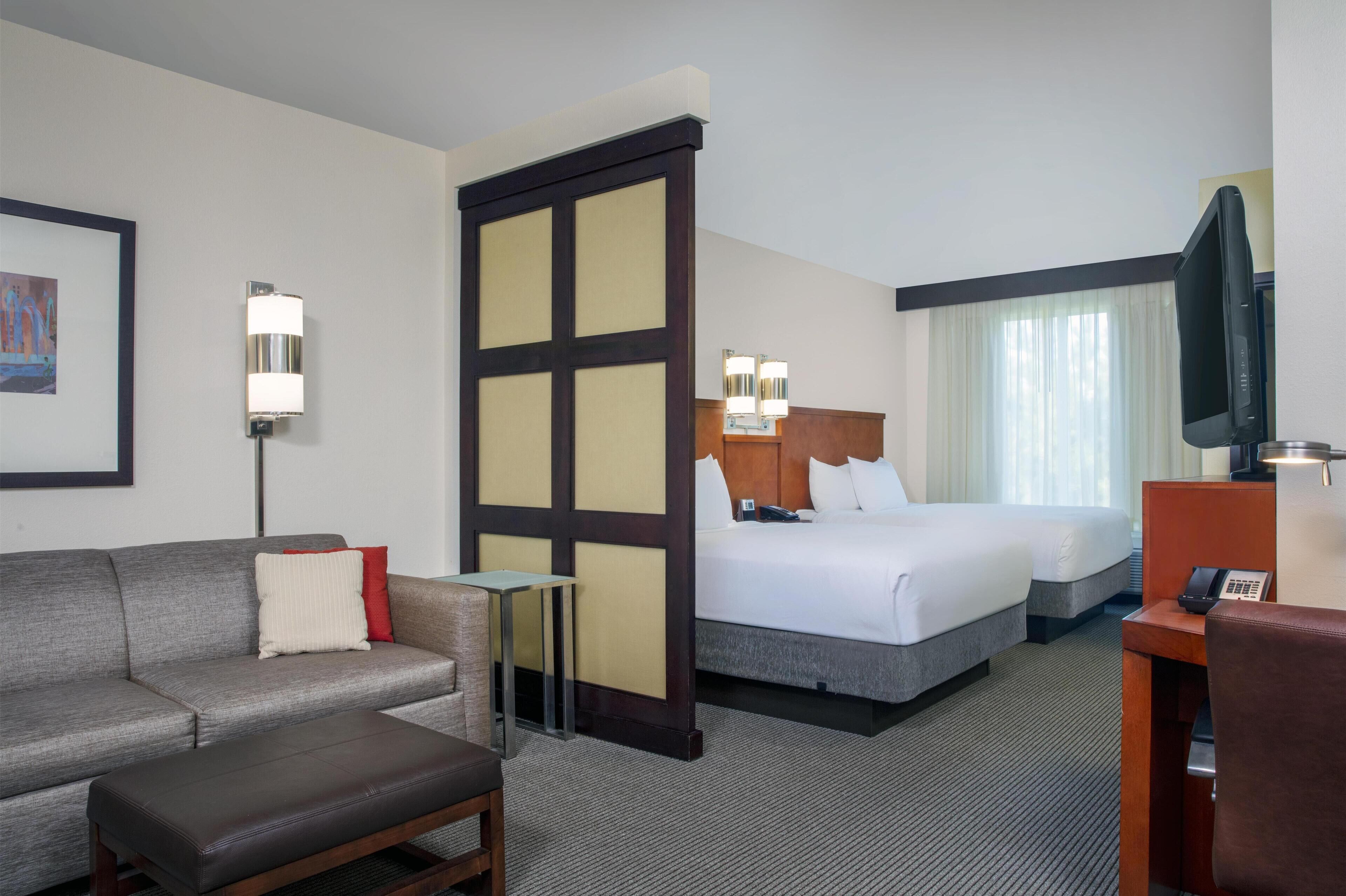 A hotel room with a sofa, a bed, a desk, a TV, and a window with curtains.