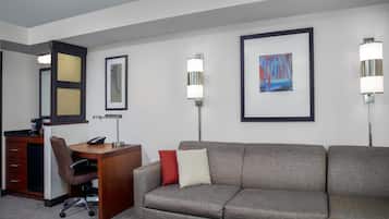 Habitación de hotel con escritorio, silla de oficina, sofá y dos lámparas de pared.