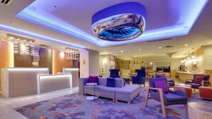 A modern hotel lobby with a reception desk, seating area, and a large decorative ceiling feature.