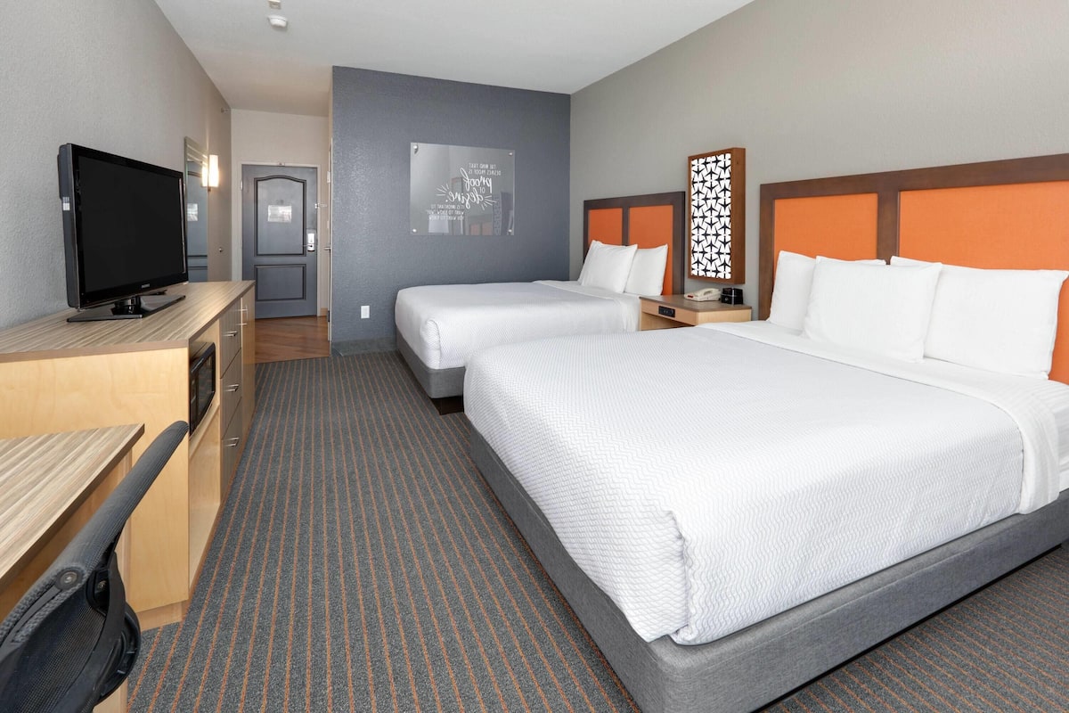 A hotel room with two beds, a desk with a television, a small kitchenette, and a carpeted floor.