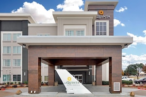 Een moderne hotelentree met een opvallend 'La Quinta' bord, een overdekte doorgang en een parkeerplaats.
