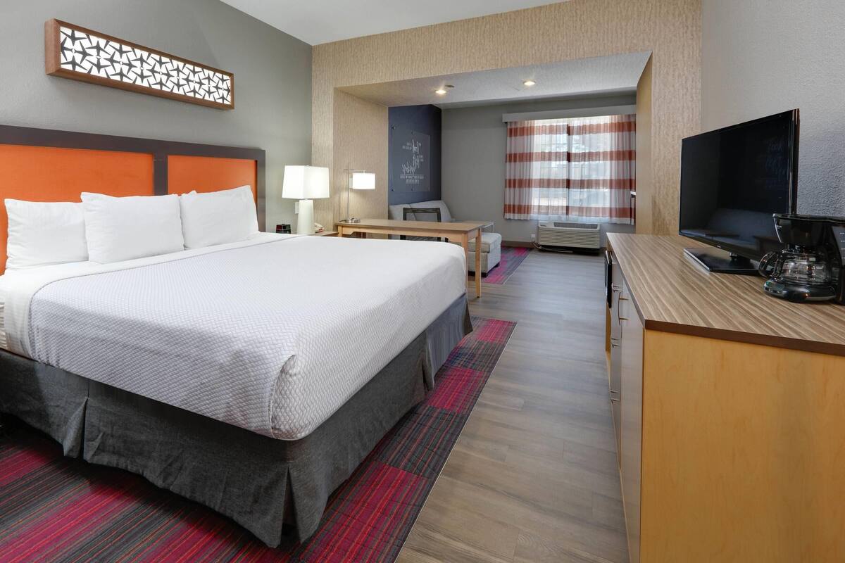 A hotel room with a large bed, a desk with a television, and a seating area with a chair and table.