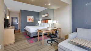 A hotel room with a bed, desk, chair, and a sofa.