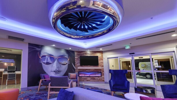 A modern lobby with a large circular ceiling feature, a flat-screen TV, seating areas, and a glass door entrance.