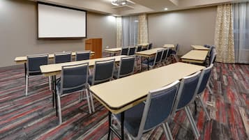 A conference room with a large screen, multiple tables, and chairs.