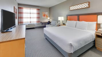 Habitación de hotel con una cama grande, un escritorio, una televisión y una ventana con cortinas.