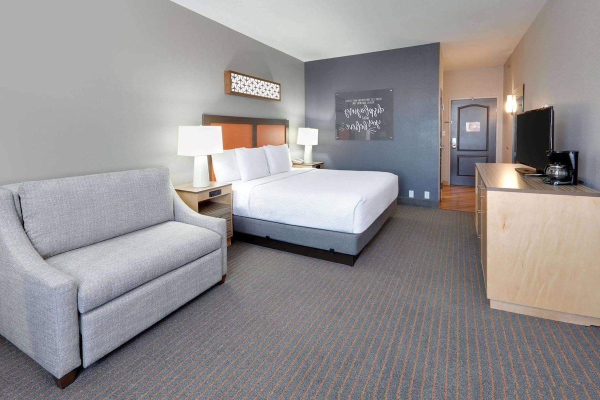 A hotel room with a bed, a sofa, a desk with a coffee maker, and a TV.