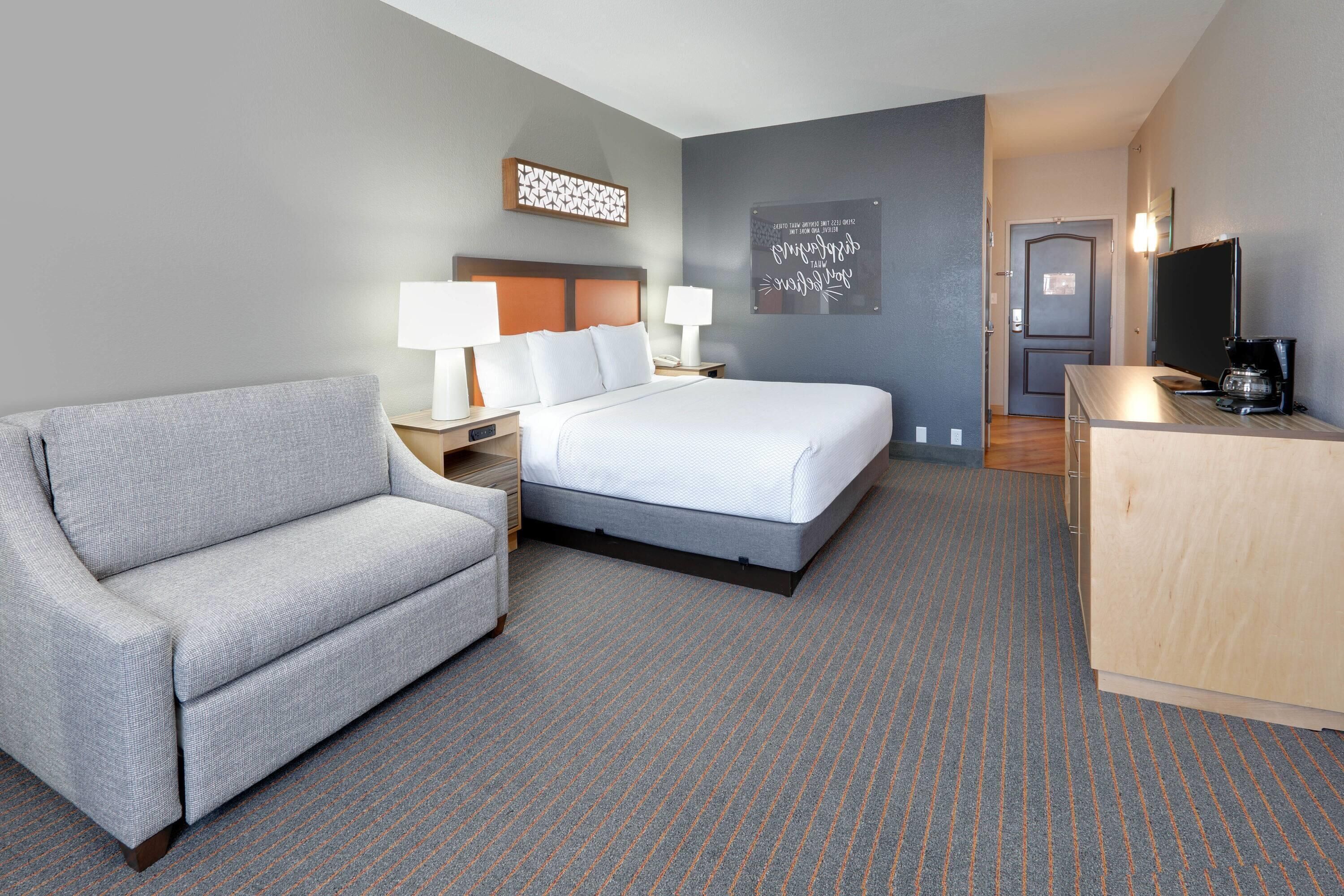 A hotel room with a bed, a sofa, a desk with a coffee maker, and a TV.
