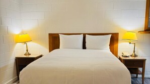 A neatly arranged hotel room with a large bed, two bedside tables with lamps, and a wooden headboard.