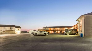 A parking lot with several vehicles, a building with multiple windows and a flat roof, and a clear sky.