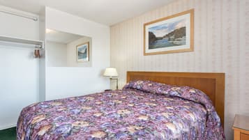 A bedroom with a floral bedspread, a wooden headboard, a nightstand with a lamp, a framed picture on the wall, and a mirror above the bed.