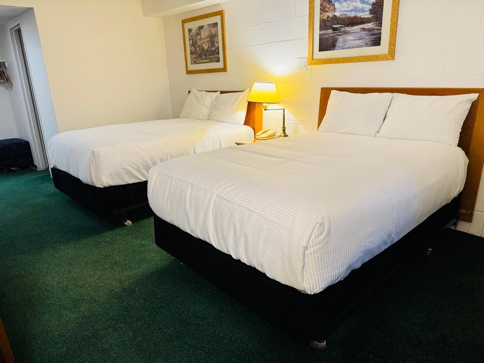A hotel room with two beds, a green carpet, and a framed picture on the wall.