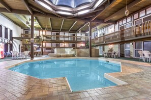 An indoor swimming pool with a tiled floor, wooden deck, and multiple seating areas with chairs and tables. - Moosejaw Inn (Moose Jaw)