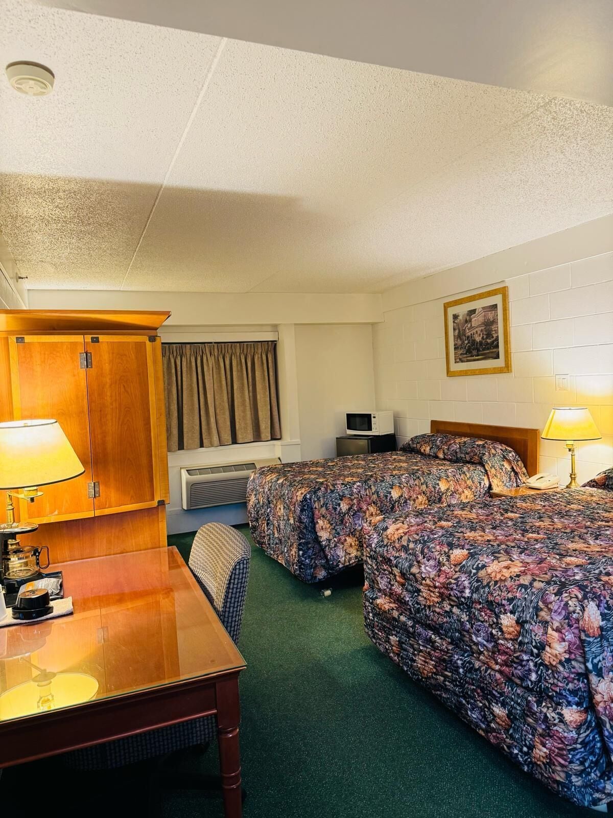 A hotel room with two beds, a desk, a chair, a TV, and a picture on the wall.